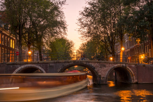 istock Sunset on the Amsterdam Canal and a Boat Under the Bridge 1369593442