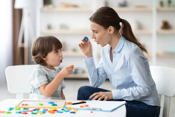 Photo of Female speech therapist curing child's problems and impediments. Little boy learning letter O with private tutor