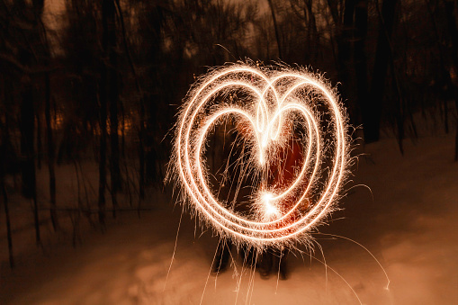 Couple made heart shape with bengal fires. Bright sparkles shines in winter evening. Valentine day celebration. Freeze light.