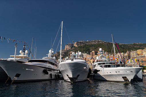 A lot of huge yachts are in port of Monaco at sunny day, Monte Carlo, mountain is on background, glossy board of the motor boat, megayachts are moored in marina, sun reflection on glossy board. High quality photo