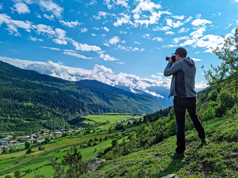 A male photoprapher enjoying the amazing view on the valley in Mestia in the Greater Caucasus Mountain Range, Upper Svaneti, Country of Georgia. Clouds cover the snow capped mountain peaks.Outdoor