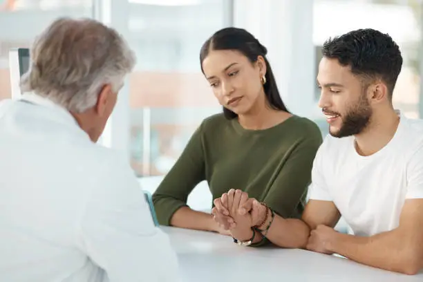 Photo of Shot of a young couple sitting with their obstetrician and holding hands during a consultation in the clinic