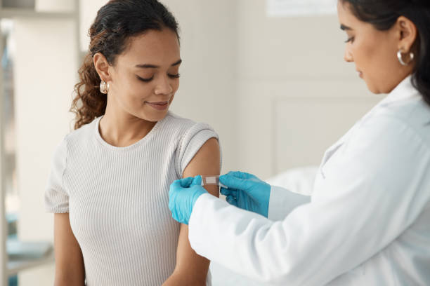 aufnahme einer jungen ärztin, die ein pflaster anwendet, nachdem sie ihre patientin während einer konsultation in der klinik injiziert hat - asian ethnicity doctor patient healthcare and medicine stock-fotos und bilder