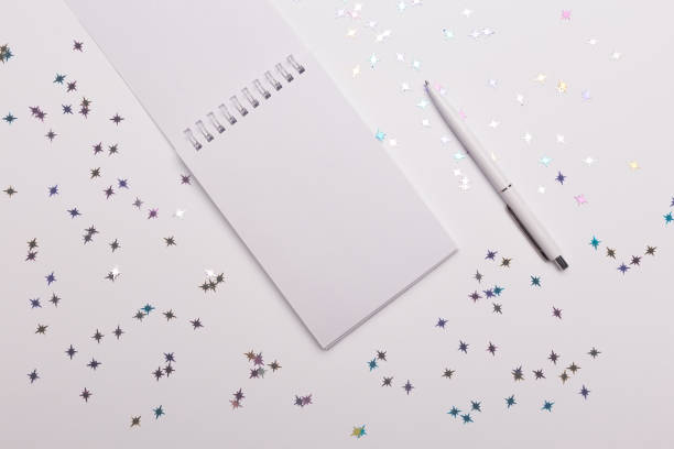 istock White blank notebook with white pen on white desk background. 1369605937