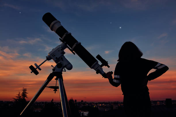 istock Girl with astronomical telescope stargazing under twilight sky. 1369606065