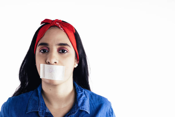 hispanic woman with tape on her mouth concept of feminism, on white background. latin woman representing the concept of feminism in the studio with white background speaking with forked tongue stock pictures, royalty-free photos & images