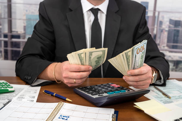 istock A handsome man in a black stylish suit at a spacious table counts dollars and fills out forms. 1369611377