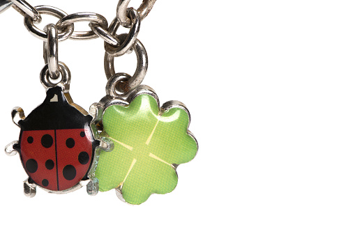 Close up of silver metal chain with two small lucky charms on it a ladybug and a four leaf clover made of silver on white background