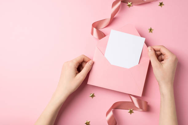 first person top view photo of valentine's day decor woman's hands holding open pink envelope with paper card golden stars and pink silk curly ribbon on isolated pastel pink background with copyspace - writing letter correspondence women imagens e fotografias de stock