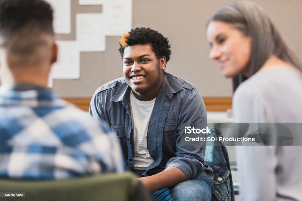 Unrecognizable teacher smiles as teen welcomes new student The unrecognizable female teacher is happy when the teenage boy smiles and welcomes an unrecognizable male student. Mental Health Stock Photo