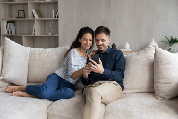 istock Happy couple using smartphone, relaxing on couch together 1369617659