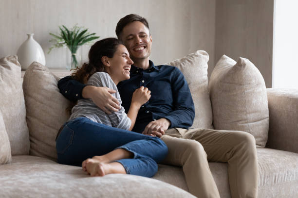 istock Laughing couple hugging, relaxing sitting on couch together 1369617664