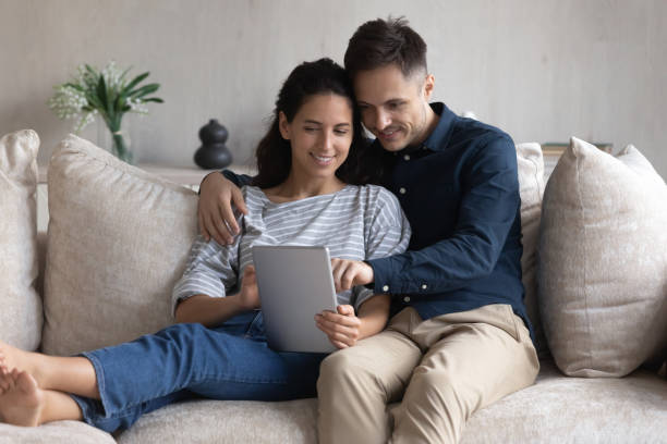 istock Smiling young couple using tablet together, sitting on couch 1369617665