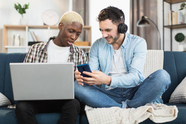 istock Multiracial same sex couple resting on couch with gadgets 1369618100