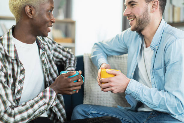 istock Two loving men drinking tea and talking on couch 1369619058
