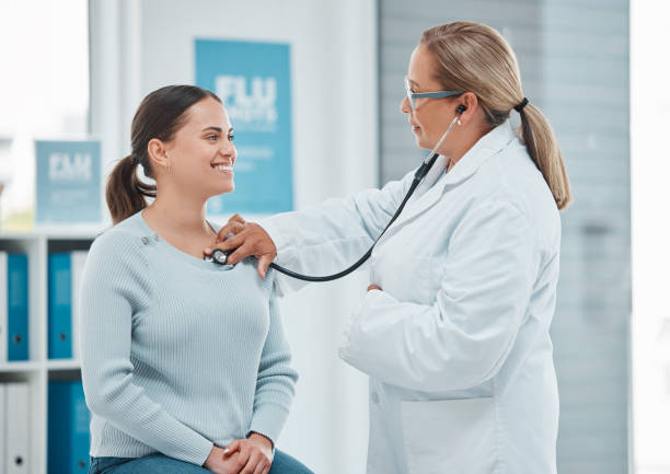 foto de un médico examinando a un paciente con un estetoscopio durante una consulta en una clínica - 50s adult doctor equipment fotografías e imágenes de stock