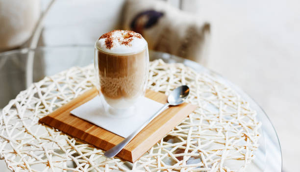 hot latte or cappuccino coffee on table in cafe or kitchen near the window with copy space.morning coffee latte with milk and chocolate on top in double walled glass on serving board with spoon. - cafe macchiato latté heat coffee imagens e fotografias de stock