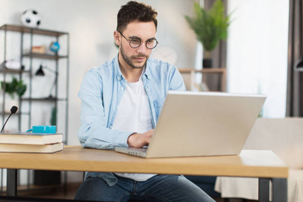 istock Man in eyewear sitting at desk and working on laptop 1369620779