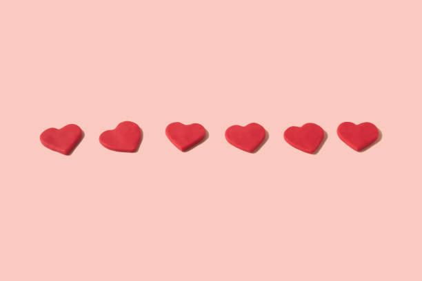 istock Lined up and centered red hearts made from modeling clay on a pastel pink background with copy space 1369621881