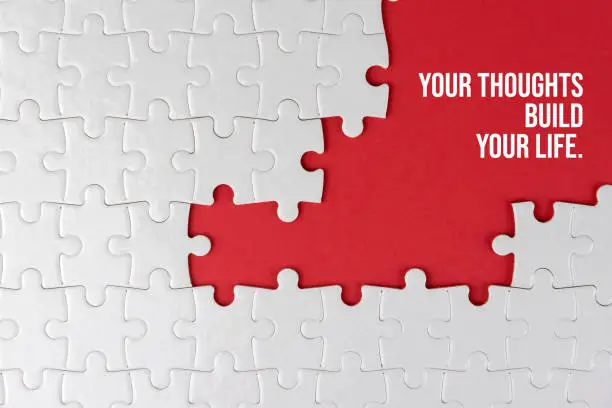 Inspirational motivational quote - Your thoughts build your life. With white jigsaw puzzle with some missing pieces on red background. Business motivation words with puzzle jigsaw backgrounds.