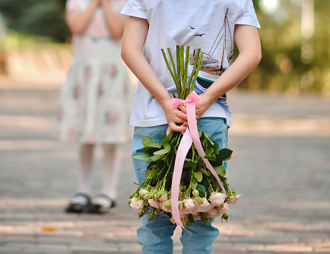 A little boy holds bouquet of flowers behind his back. Surprise gift for the girl on March 8, Valentine's Day. Flowers in the hands of a child boy