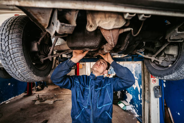 automechaniker, der das auto in einer werkstatt untersucht - maintenance engineer car lamp protective workwear stock-fotos und bilder