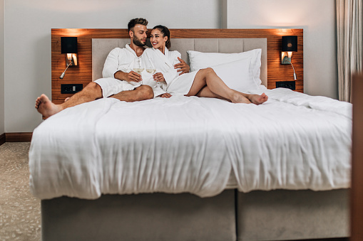 A young couple in bathrobes lie on the bed of a hotel room, relax and enjoy.