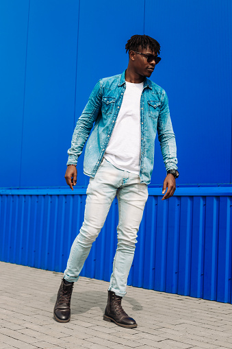 Fashion portrait of stylish handsome curly African man in sunglasses walking through the streets of urban background, Man in casual clothes near blue wall