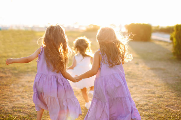 Sisters in similar outfits holding hands and running on grass while playing in summer park together