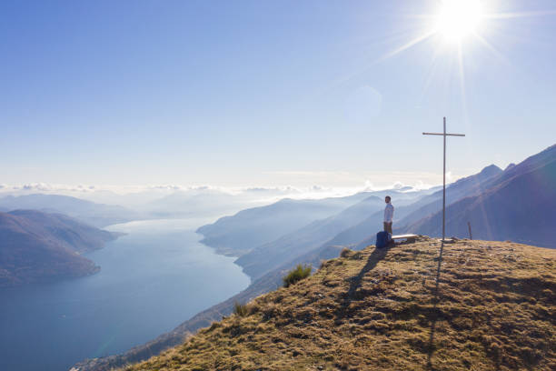 Man takes a moment to enjoy the views from mountain top, aerial view. Hiker looks at distant mountain range above lake
