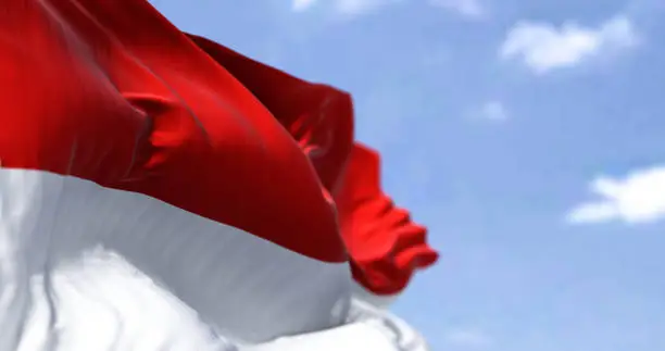 Photo of Detail of the national flag of Indonesia waving in the wind on a clear day.