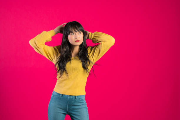 Confident woman hand on hair standing against pink background.