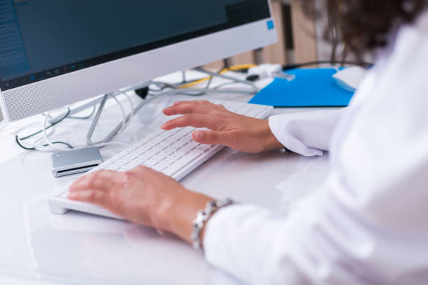 istock Close up hands of a female physician ( nurse ) typing on her white keyboard while sitting on a white desk in a hospital lobby. 1369646657