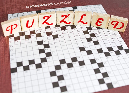 Unfilled crossword puzzle with the word puzzled in wood letters spelled out on top of puzzle. A concept of being puzzled by a challenge.