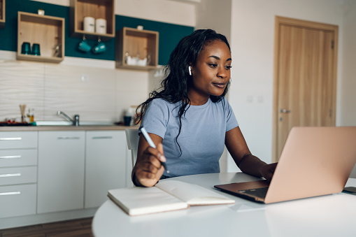 Young african american woman making video call with laptop in a kitchen at home and having an online web conference with her colleagues from work. Social distance and modern technology.