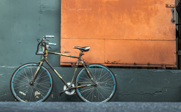 倉庫の緑の壁を持つスチールオレンジのドアの前に1台の自転車。 - bicycle wall green single object ストックフォトと画像