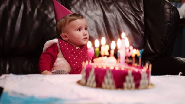 One year birthday party of a baby girl,she is sitting in front of the birthday cake with  candles. Creating memories.