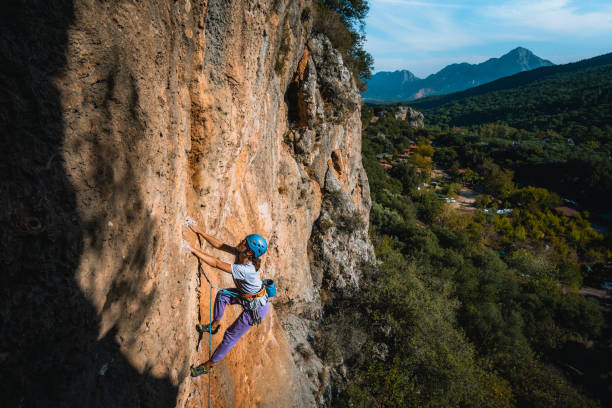 climber ascends steep rock wall above lush valley - leadership risk cliff mountain climbing imagens e fotografias de stock