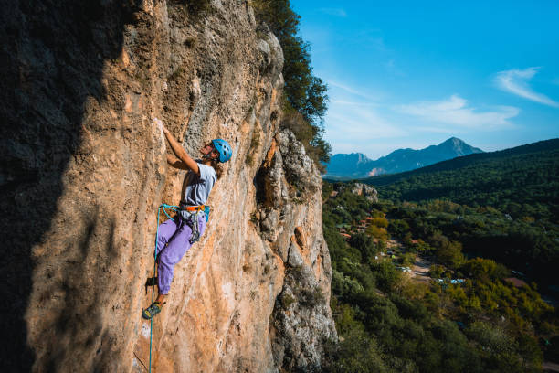 climber ascends steep rock wall above lush valley - leadership risk cliff mountain climbing imagens e fotografias de stock