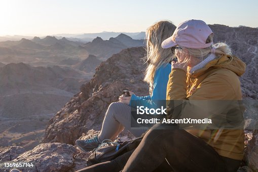istock Mother and adult daughter drink hot beverage on mountain summit 1369657144