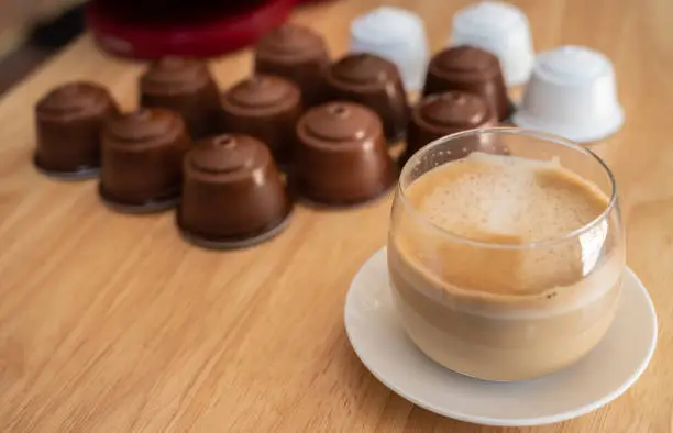 Photo of A cup of latte coffee with group of coffee capsule (or pods) on wooden table.