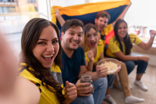 Latin American roommates having a great time watching a soccer game and taking a selfie while looking at camera smiling - Lifestyles