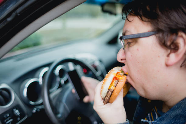 istock Man Using Cell Phone While Eating A Hamburger In His Car 1369663760
