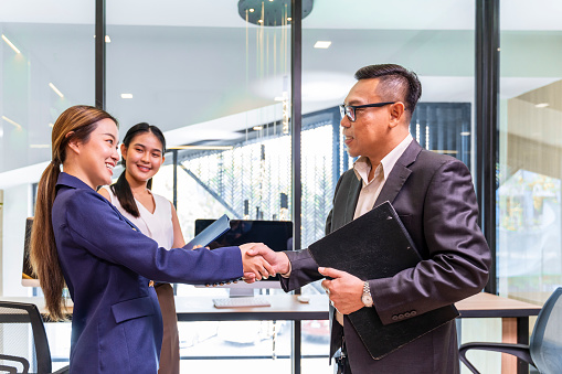 Asian business CEO congratulate female employee for the outstanding achievement of her team performance by shaking hand in modern office workplace