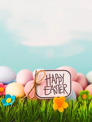 Easter background with a collection of brightly colored Easter eggs in grass with flowers and HAPPY EASTER sign