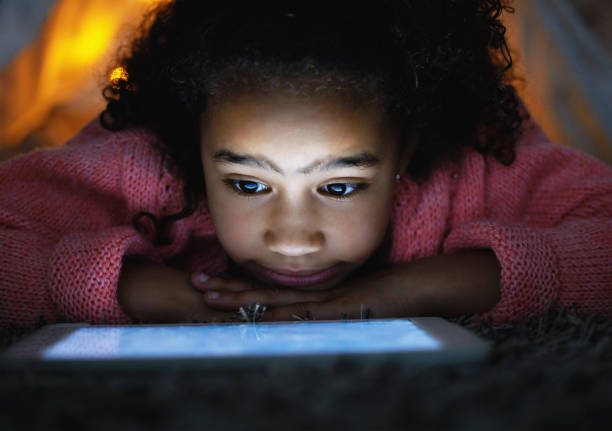 foto de uma menina adorável usando um tablet digital durante a hora de dormir em casa - dark little girls child happiness - fotografias e filmes do acervo