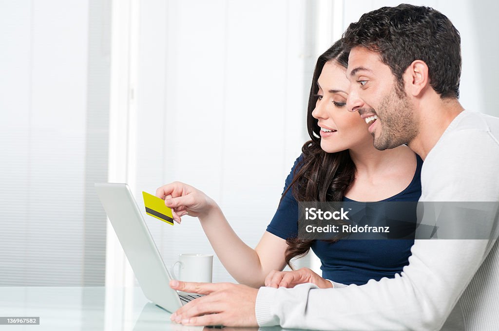 Surpised couple internet shopping Happy surprised couple looking and buying online with credit card at home. 20-29 Years Stock Photo