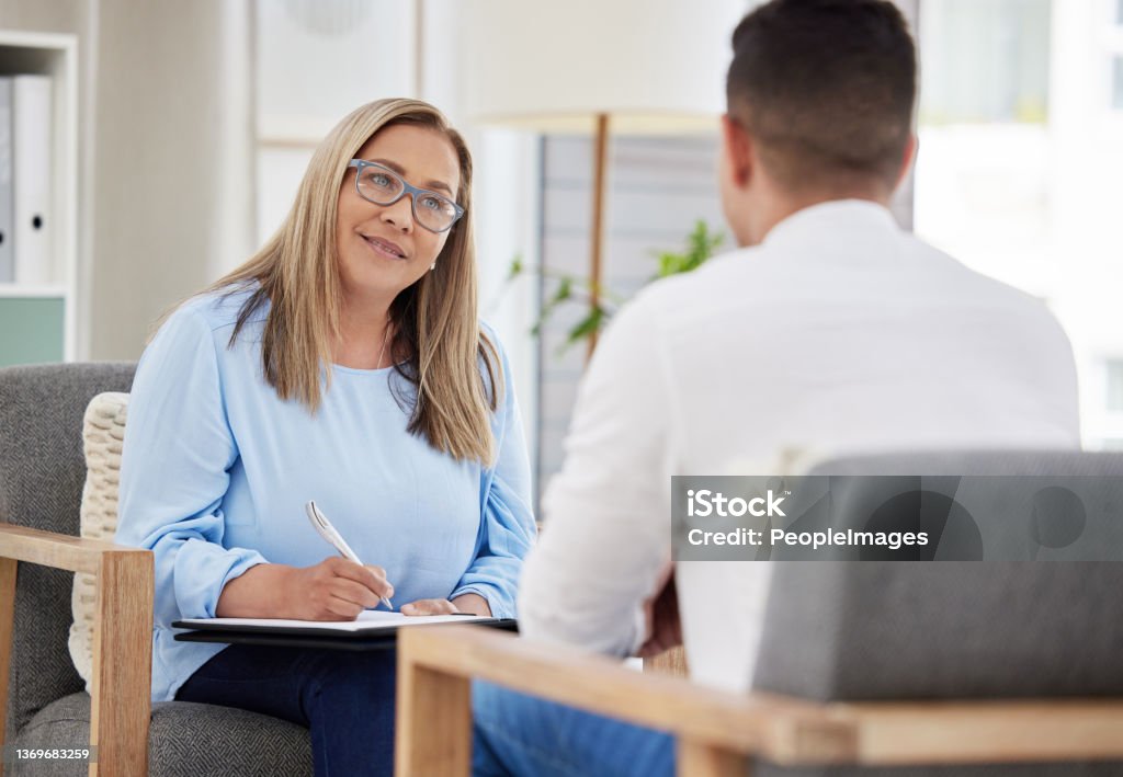 Shot of a mature psychiatrist sitting with her patient during a consultation in her clinic When did you start feeling this way? Mental Health Professional Stock Photo