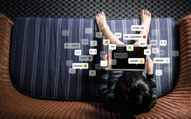 istock Top view of little Asian boy child using computer tablet alone on sofa in dark room with cyberbullying emoticon. 1369689376