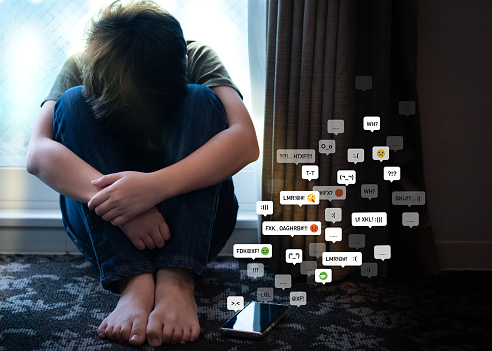 Portrait of a teenager boy sitting alone in the room with his smartphone, feeling hurt, anxiety and depress from cyberbullying on social media. Technology and mental health problems with children concept.